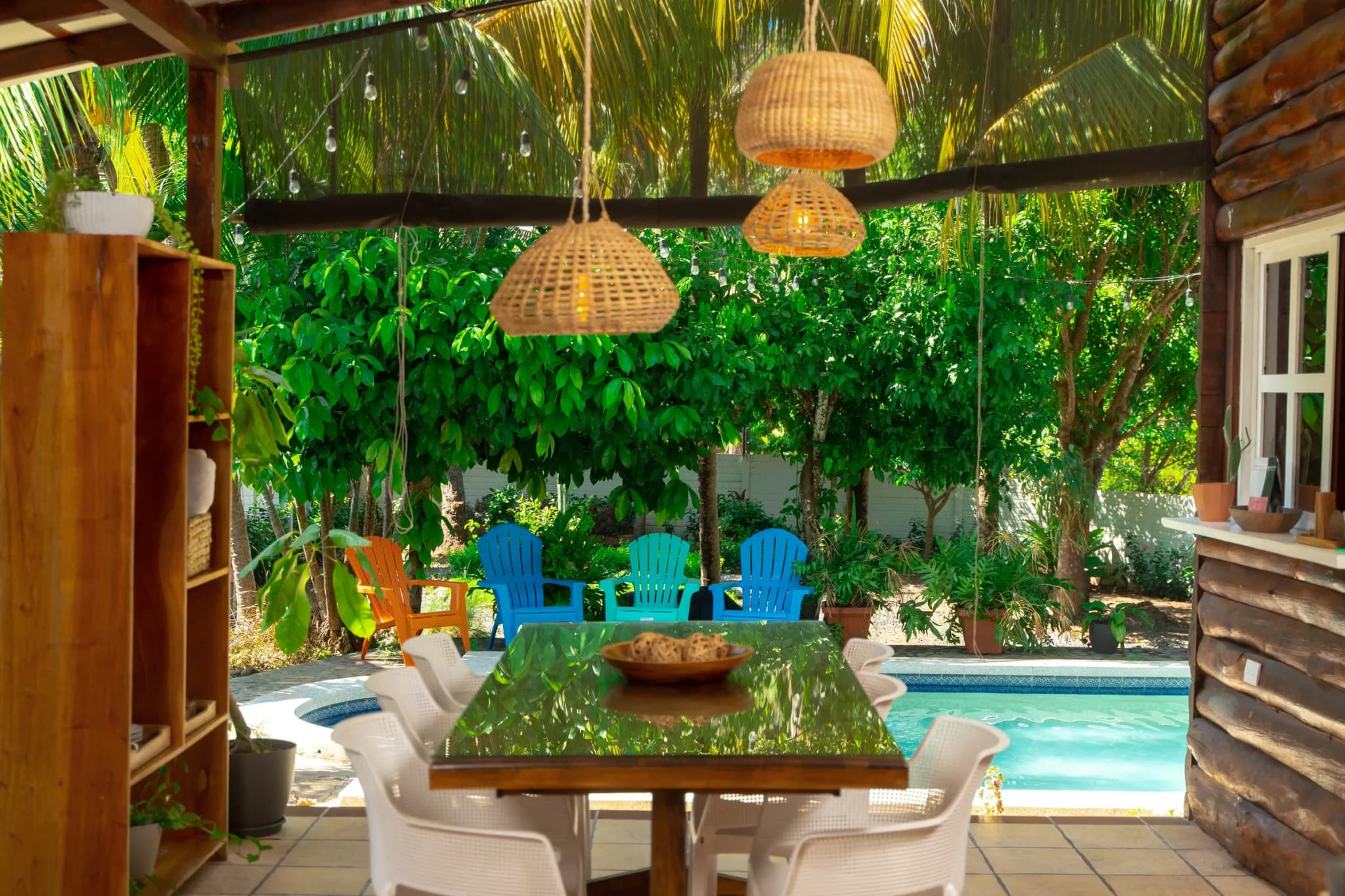 Comedor bajo la palapa con lámparas tejidas y la piscina al fondo